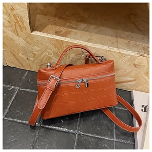 Detailed view of orange crocodile-patterned crossbody bag on stone and wood background
