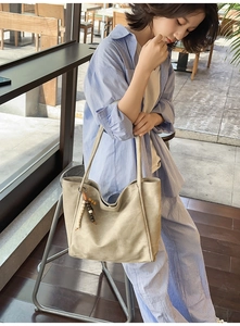 Beige tote bag detail featuring a smooth matte texture and a decorative beaded charm