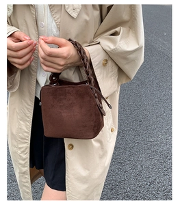 Detail of a dark brown suede bucket bag featuring a unique braided handle held by a model