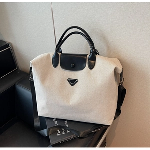 Detail of canvas tote bag with black leather trim and triangle metal logo on front
