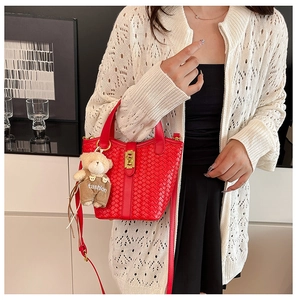 Dettaglio della borsa a secchiello rossa intrecciata con fibbia oro e ciondolo a orsetto