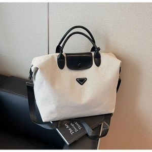 Close-up of canvas tote bag with black leather straps and triangular metal logo plate