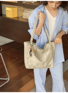 Detail of light grey tote bag with wooden bead charm on a person in casual setting