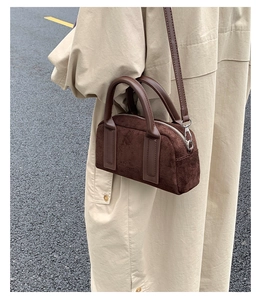 Detail of dark brown suede handbag showing soft texture and crossbody strap on beige coat