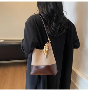 Détail du sac seau en daim kaki et cuir marron avec pompon en perles et finitions dorées