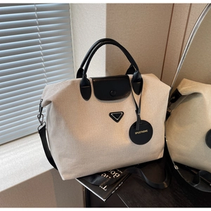 Close-up of beige canvas travel tote with black leather handles and metal triangle detail