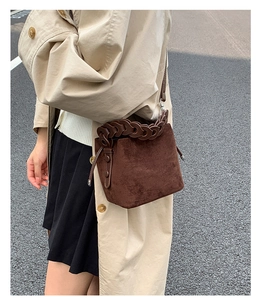 Detail of dark brown suede bucket bag with woven handle and beige trench coat style