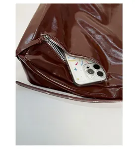 Detail of the front zipper pocket on a glossy dark tote bag with striped lining