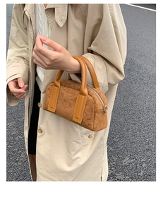 Detailed view of a brown suede bowling bag with smooth leather handles and silver zipper closure