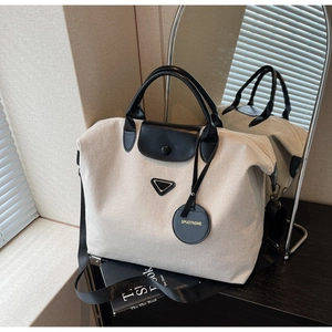 Detailed close-up of beige canvas tote bag showing black leather handles and metal studs