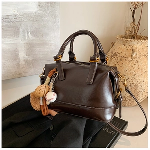 Detailed view of brown leather Boston bag with unique baseball charm and shoulder strap