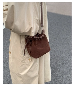 Detail of dark brown suede bucket bag featuring a textured braided top handle