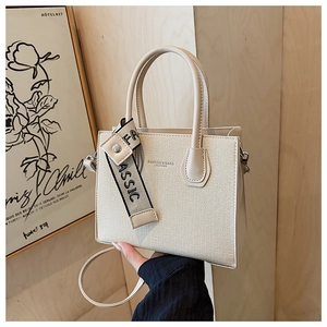 Détail du sac carré en toile beige avec garniture en cuir et pendentif ruban classique