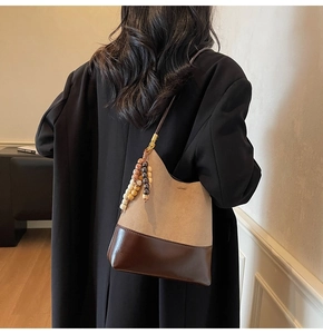 Détail d'un sac hobo avec cuir bicolore et breloque en perles de bois porté par un modèle