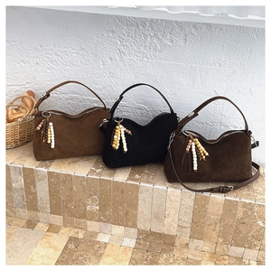 Close-up of three vintage suede pillow bags with colorful wooden bead tassels on stone steps