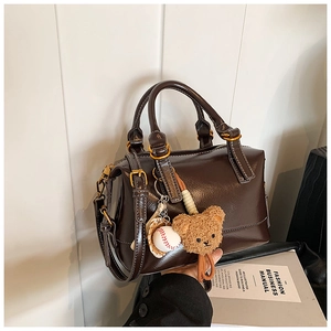 Detail of dark brown leather Boston bag with plush bear charm and gold hardware