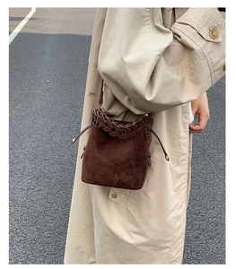 Brown suede bucket bag with chain detail and drawstring, shown on a stylish trench coat