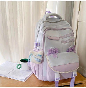 Detail of lavender school backpack featuring lace trim, bow ribbons, and a plush bear charm