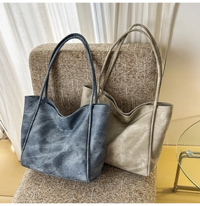 Detail view of large vegan leather tote bags in vintage blue and khaki on a woven chair