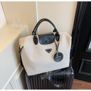 Macro detail of canvas travel tote with leather trim resting on a black suitcase