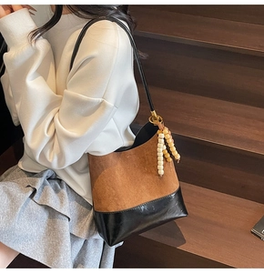 Détail du sac bandoulière rétro en daim avec surpiqûres contrastées et pompon en perles