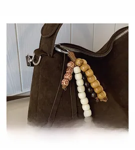 Detail of dark brown suede shoulder bag with ethnic wooden bead charm and silver hardware