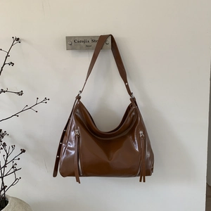 Detail of brown hobo bag with glossy finish and decorative vertical zippers