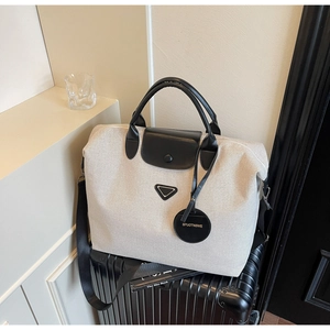 Detail of canvas travel tote with black leather handles and logo plaque on luggage