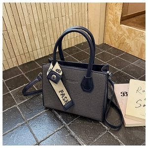 Détail du sac Boston avec finitions en cuir, doubles poignées et ruban de mode
