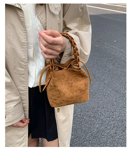 Close-up of brown suede bucket bag featuring a vintage braided leather handle and drawstring