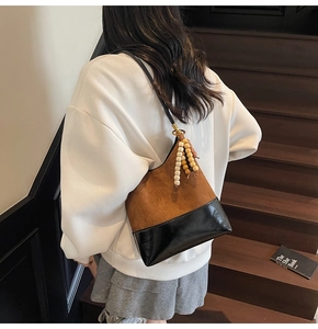 Détail du sac seau bicolore en daim marron et cuir noir avec pendentif décoratif