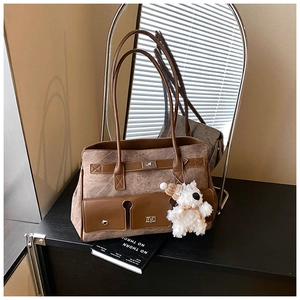 Detail of a brown leather tote bag featuring two front pockets and a cute plush bear charm