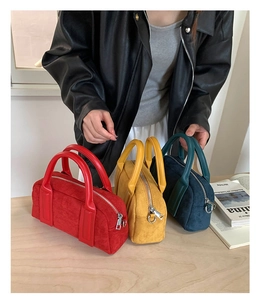 Detailed view of suede bowling bags in red, yellow and cyan on a wooden surface