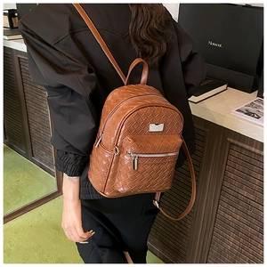 Dettaglio dello zaino in pelle marrone intrecciata con cerniera argentata e logo metallico