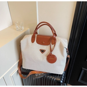 Detail of canvas travel tote on suitcase showing leather handles and metal triangle plaque