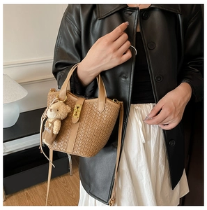 Dettaglio borsa a secchiello intrecciata marrone con texture e ciondolo a forma di orsetto