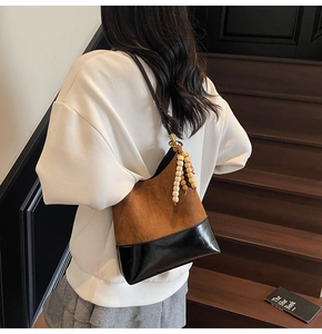 Détail du sac cabas en daim marron avec base noire et breloque en perles de bois élégante