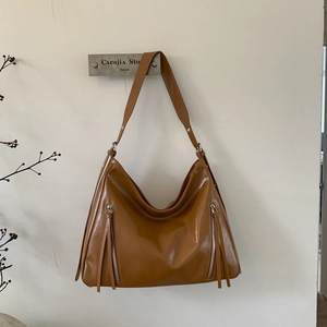Detail view of caramel brown glossy leather tote featuring long tassel and silver zipper