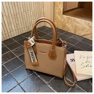 Détail du sac carré en toile marron montrant la texture, la bandoulière et les ferrures