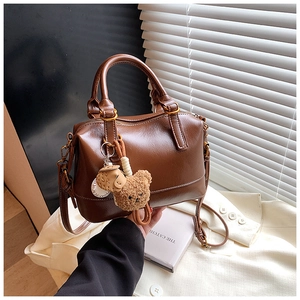 Detail of a brown leather handbag with cute plush bear charms on a white blazer background