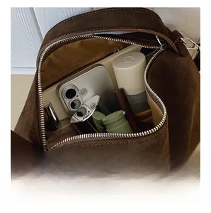 Detail view of large interior capacity of brown suede crossbody bag with items inside