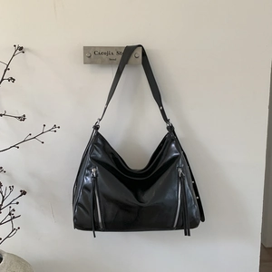 Detail of glossy black hobo bag featuring silver zippers and long leather tassels