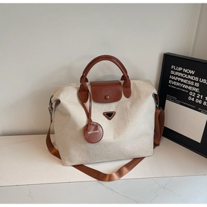Detail of canvas travel tote featuring brown leather handles and triangle metal logo