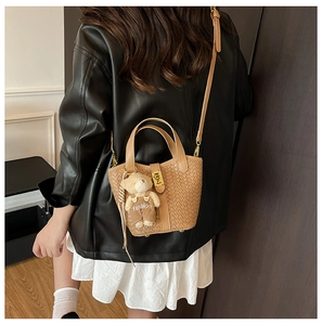 Borsa a secchiello intrecciata marrone con ciondolo a orsetto indossata da una modella