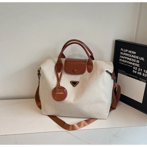 Close-up of canvas travel tote featuring brown leather handles and brand circular tag