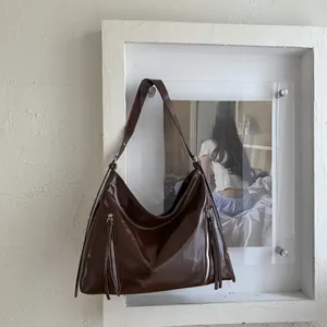 Detail of dark brown oil wax leather tote with silver zipper pulls and long tassels
