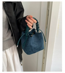Detail of dark bucket bag featuring woven handle and soft suede texture in a lifestyle setting