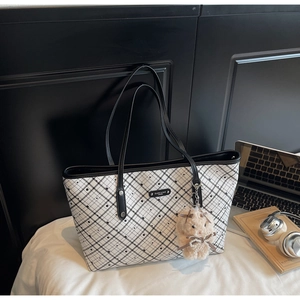 Dettaglio della borsa tote scozzese vintage con ciondolo a orsetto su letto bianco