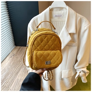 Detail of mustard yellow quilted backpack featuring suede texture and silver chain strap