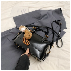 Detail of black glossy faux leather pillow bag with brown plush bear and baseball charms